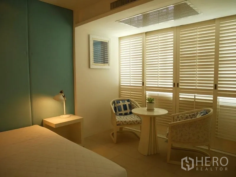 Condominium for rent in Khlong Toei, Bangkok - Bedroom corner with louvered doors and a small bistro table set.
