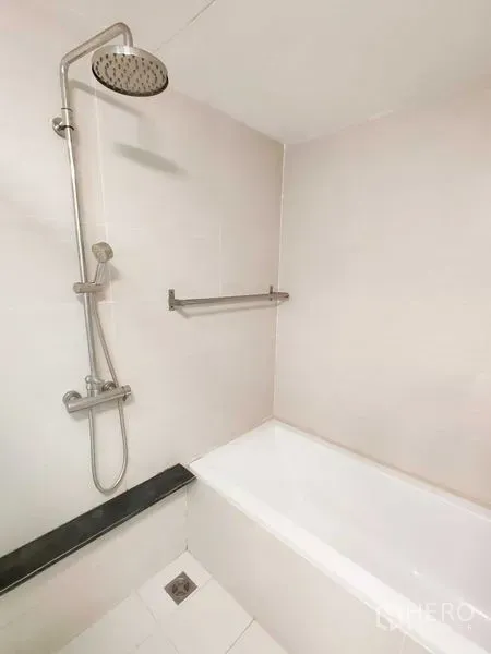 Condominium for rent in Khlong Toei, Bangkok - White bathtub with rainfall showerhead and towel rail in a tiled bathroom.