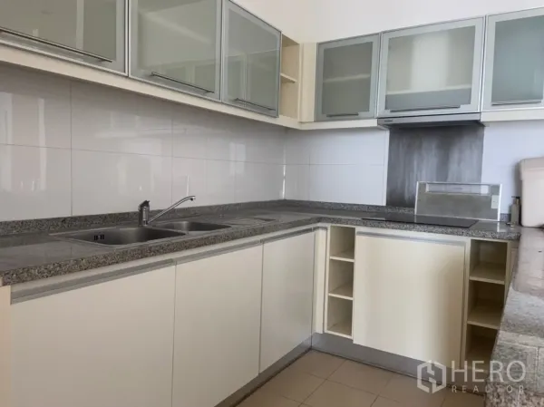 Condominium for rent or sale in Khlong Toei, Bangkok - U-shaped kitchen with granite countertops, double sink, glass-front cabinets and built-in hood.