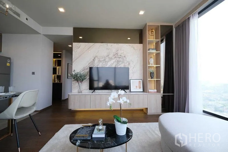 Condominium for rent in Khlong Toei, Bangkok - Living area with marble-feature TV wall, built-in shelving, and floor-to-ceiling windows.