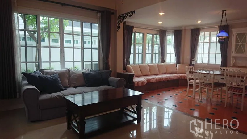 Detached House for rent in Mueang Samut Prakan, Samut Prakan - Bright living room with large corner windows, sofas, built-in window bench and recessed lighting.