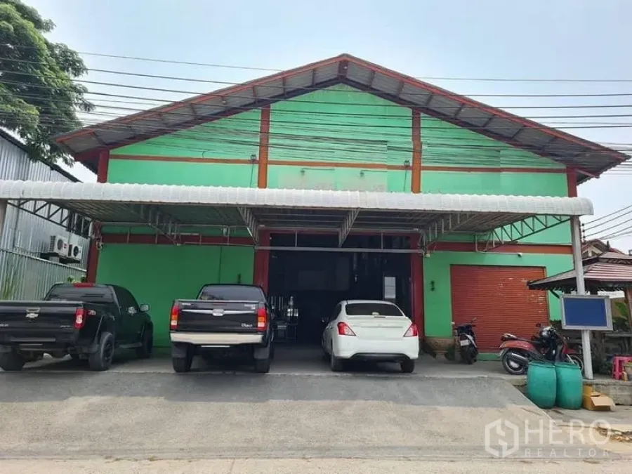 คลังสินค้า ขายในMueang Samut Prakan, Samut Prakan - ด้านหน้าโกดังสีเขียวหลังคาจั่ว ประตูกลิ้งกว้าง พร้อมลานโหลดของมีหลังคา ในเขตเมืองสมุทรปราการ