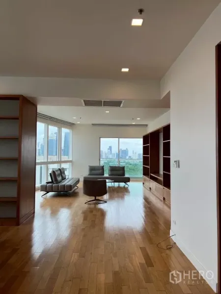 公寓 出租在Khlong Toei, Bangkok - 明亮客厅，实木地板与内置书柜，落地窗眺望曼谷天际线与公园景观。