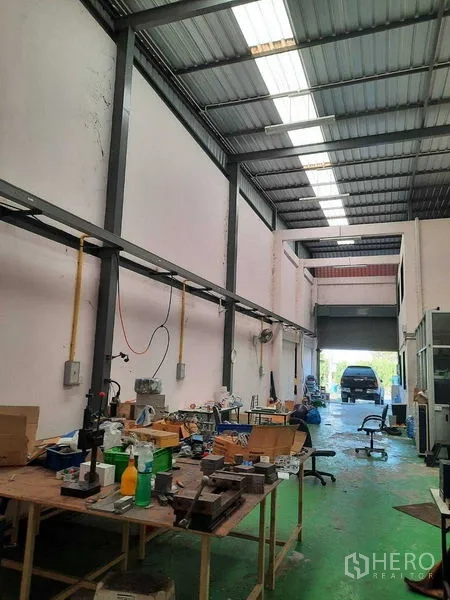 Warehouse for sale in Samut Prakan - Central work area with benches, power rails, skylights and a roll-up door at the end.