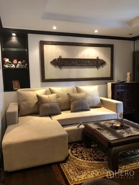 公寓 出租在Watthana, Bangkok - 温馨客厅，L 型沙发、木质茶几与墙面装饰。