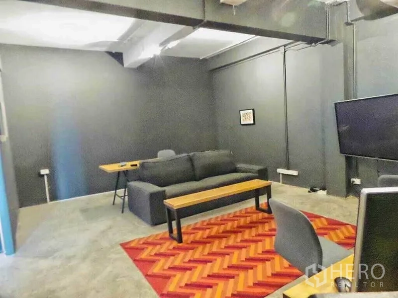 Home Office for rent or sale in Din Daeng, Bangkok - Industrial-style lounge and meeting room with dark walls, sofa, TV and red patterned rug.