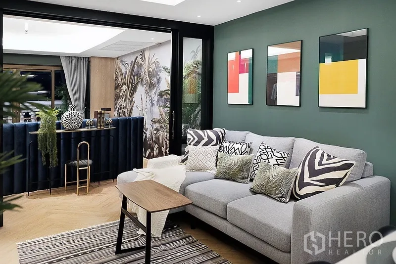 Condominium for rent in Bang Rak, Bangkok - Stylish living room with a grey sofa, patterned cushions, modern art, and sliding glass doors to a bar area and balcony.