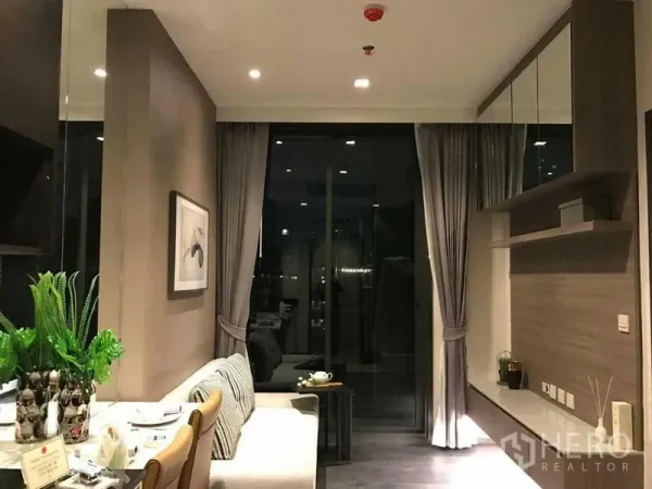 Condominium for rent in Watthana, Bangkok - Wide view of the living room at night showing built-in storage, shelving, and balcony doors.