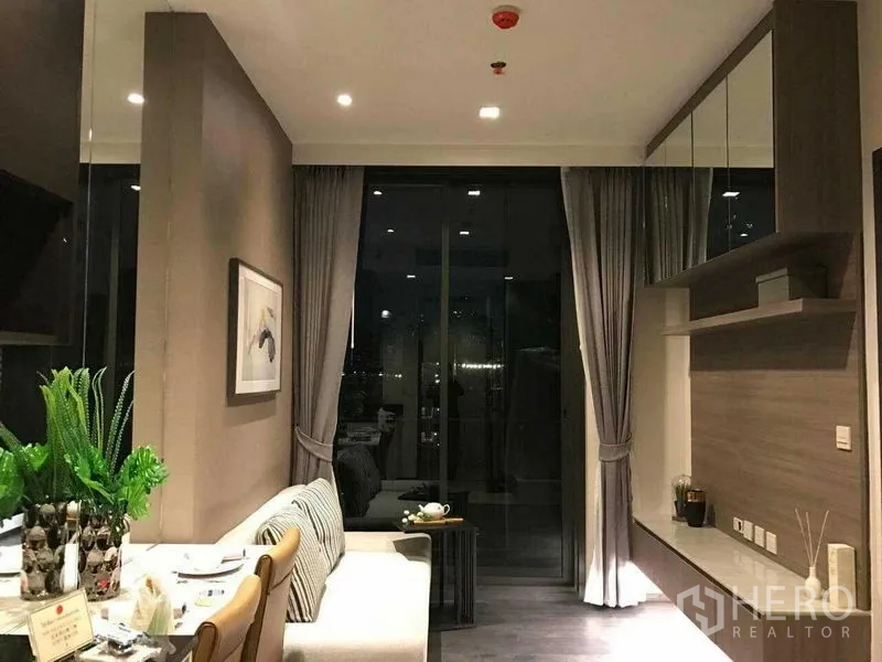 Condominium for rent in Watthana, Bangkok - Wide view of the living room at night showing built-in storage, shelving, and balcony doors.