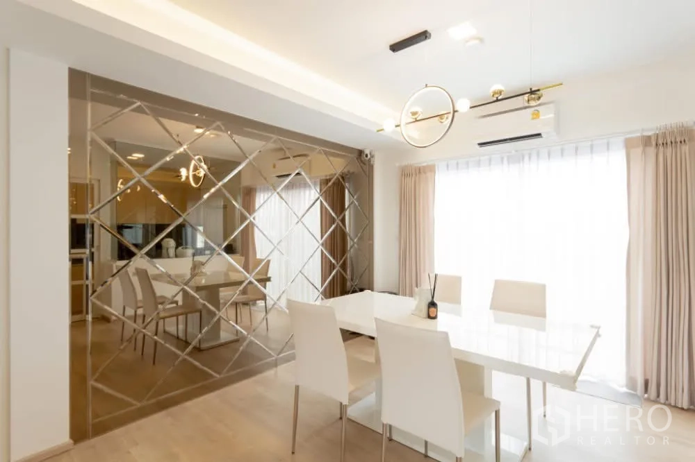 联排别墅 出租在Prawet, Bangkok - 餐区配白色餐桌、现代吊灯与菱格镜面装饰墙，采光充足。