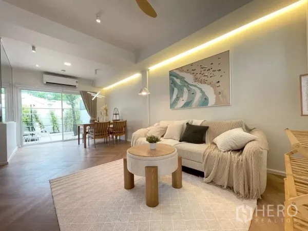 联排别墅 出租在Prawet, Bangkok - 舒适客厅与餐区，沙发、装饰画，落地推拉门通往露台。