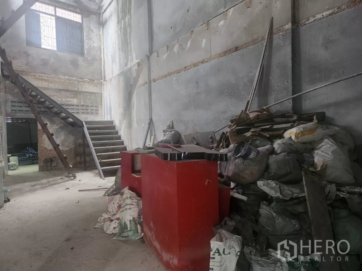 Shophouse for rent in Watthana, Bangkok - High-ceiling rear area with staircase, a red counter and renovation supplies.