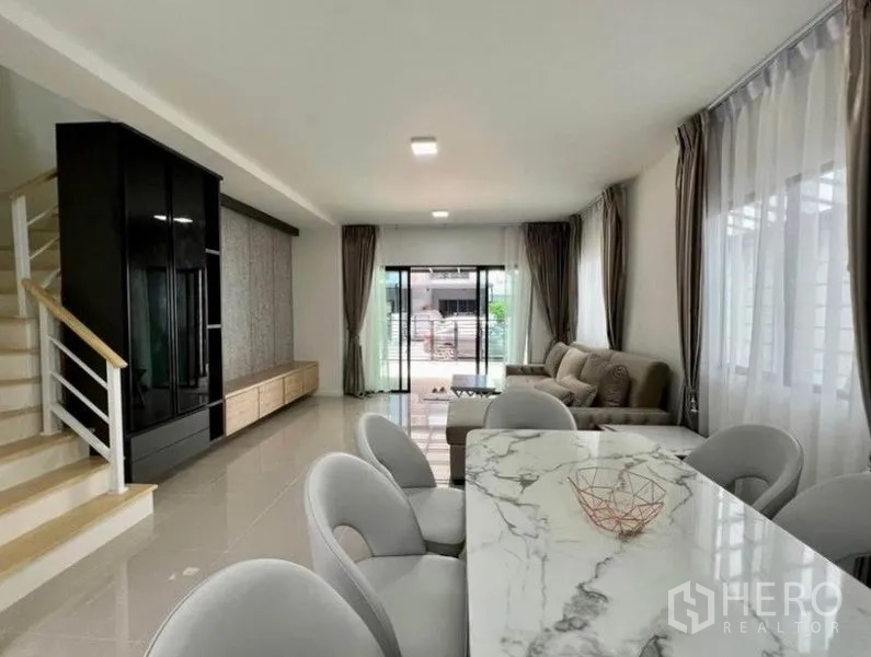 联排别墅 出租在Wang Thonglang, Bangkok - 通透明亮的客餐厅，配大理石餐桌、楼梯与落地窗滑门。