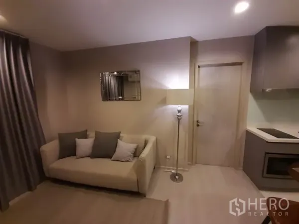 Condominium for rent or sale in Khlong Toei, Bangkok - Cozy lounge corner with sofa, floor lamp and wall mirror next to the kitchen.