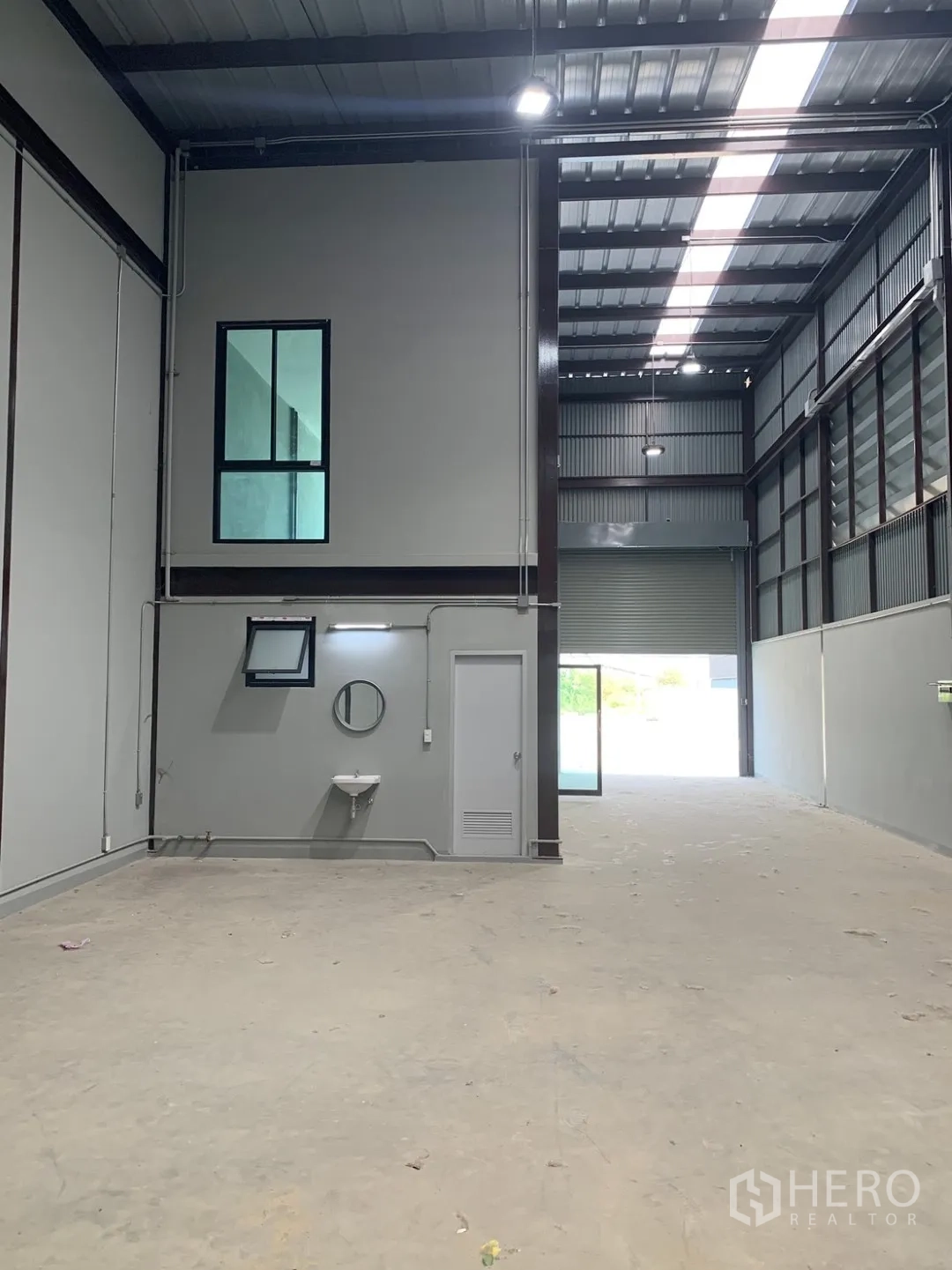 Warehouse for rent in Bang Phli, Samut Prakan - High-clearance warehouse hall with skylight panels, sink, and roller shutter entry.