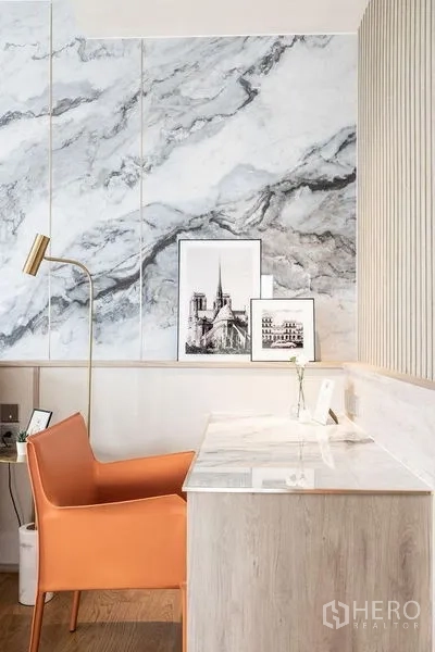 Condominium for rent in Khlong Toei, Bangkok - Stylish work nook with marble wall, white desk, and orange accent chair in a modern condominium.