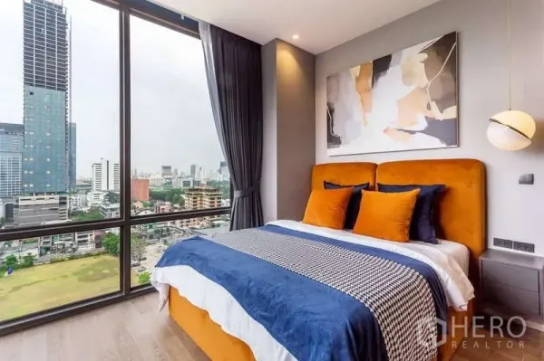 Condominium for rent in Pathum Wan, Bangkok - Second bedroom with orange headboard and panoramic city view near Lumpini Park.