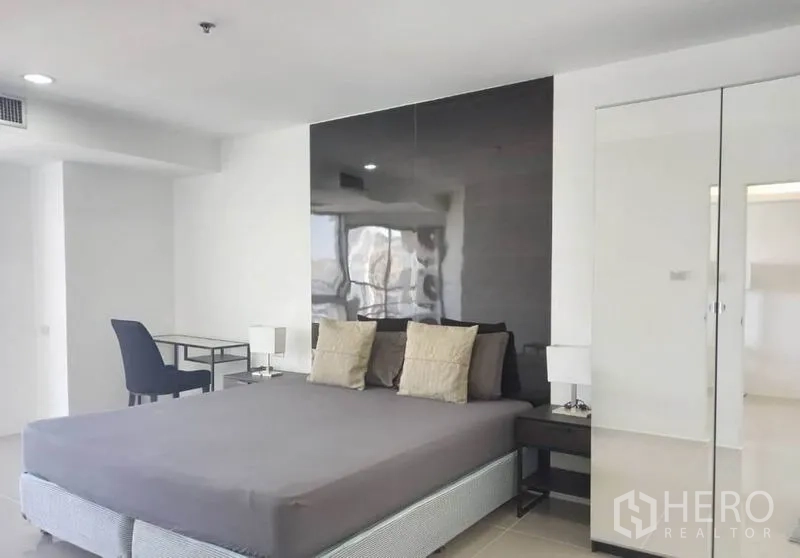 Condominium for rent in Khlong Toei, Bangkok - Bedroom angle with glossy black headboard wall, mirrored wardrobe and work desk.