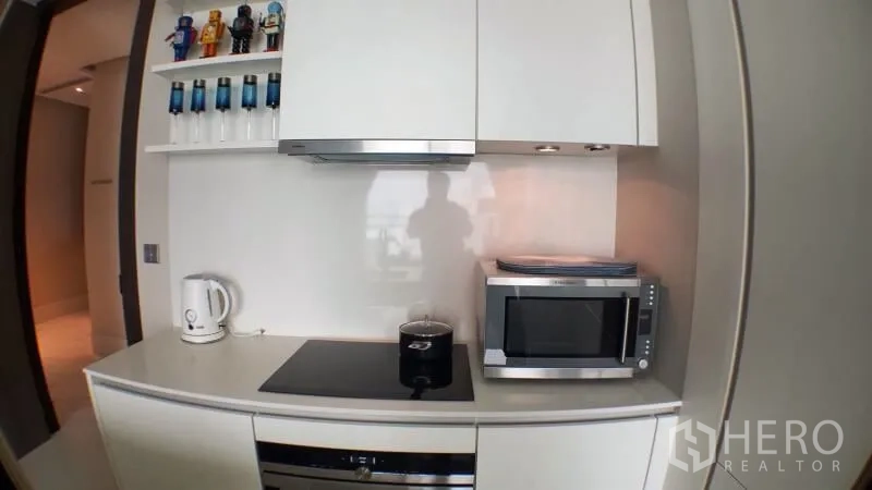 Condominium for rent in Khlong Toei, Bangkok - Compact white kitchen with cooktop, hood, microwave and open shelving.