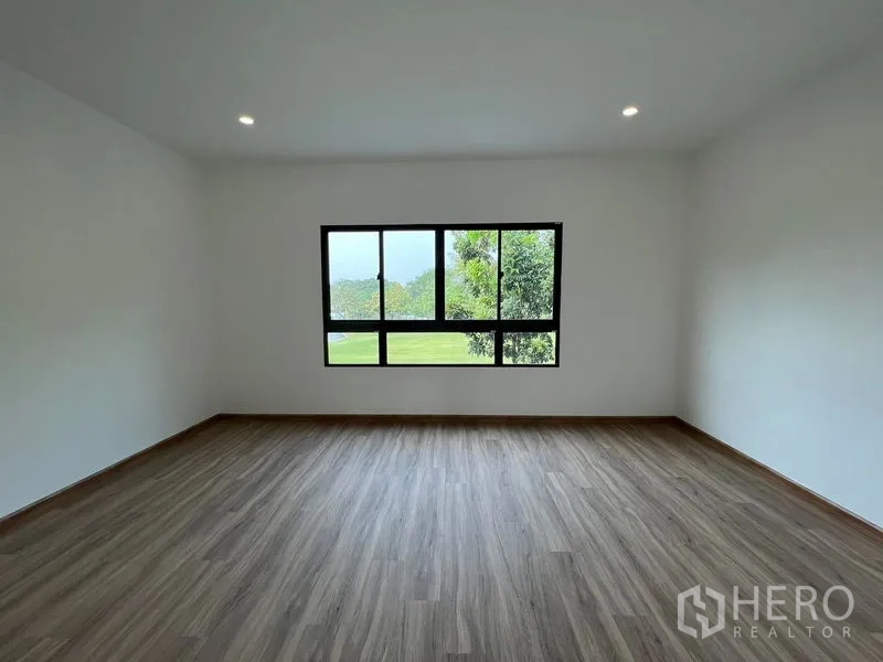 Townhouse for rent in Bang Kapi, Bangkok - Spacious bedroom with wide window and wood-look flooring overlooking greenery.