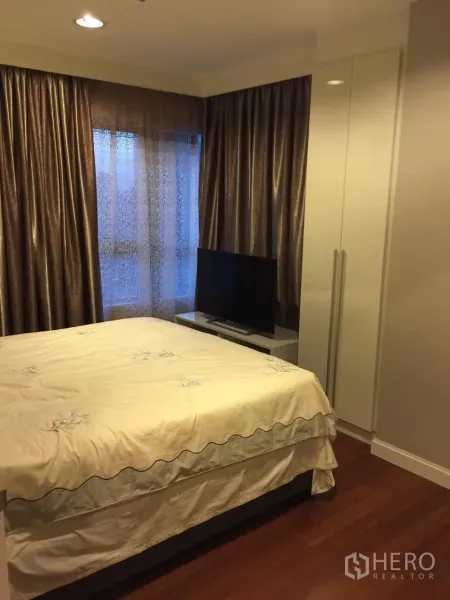คอนโด ให้เช่าในHuai Khwang, Bangkok - ห้องนอนหลักอบอุ่นด้วยเตียงคู่ ผ้าม่านสูงจรดเพดาน ตู้เสื้อผ้า และทีวี