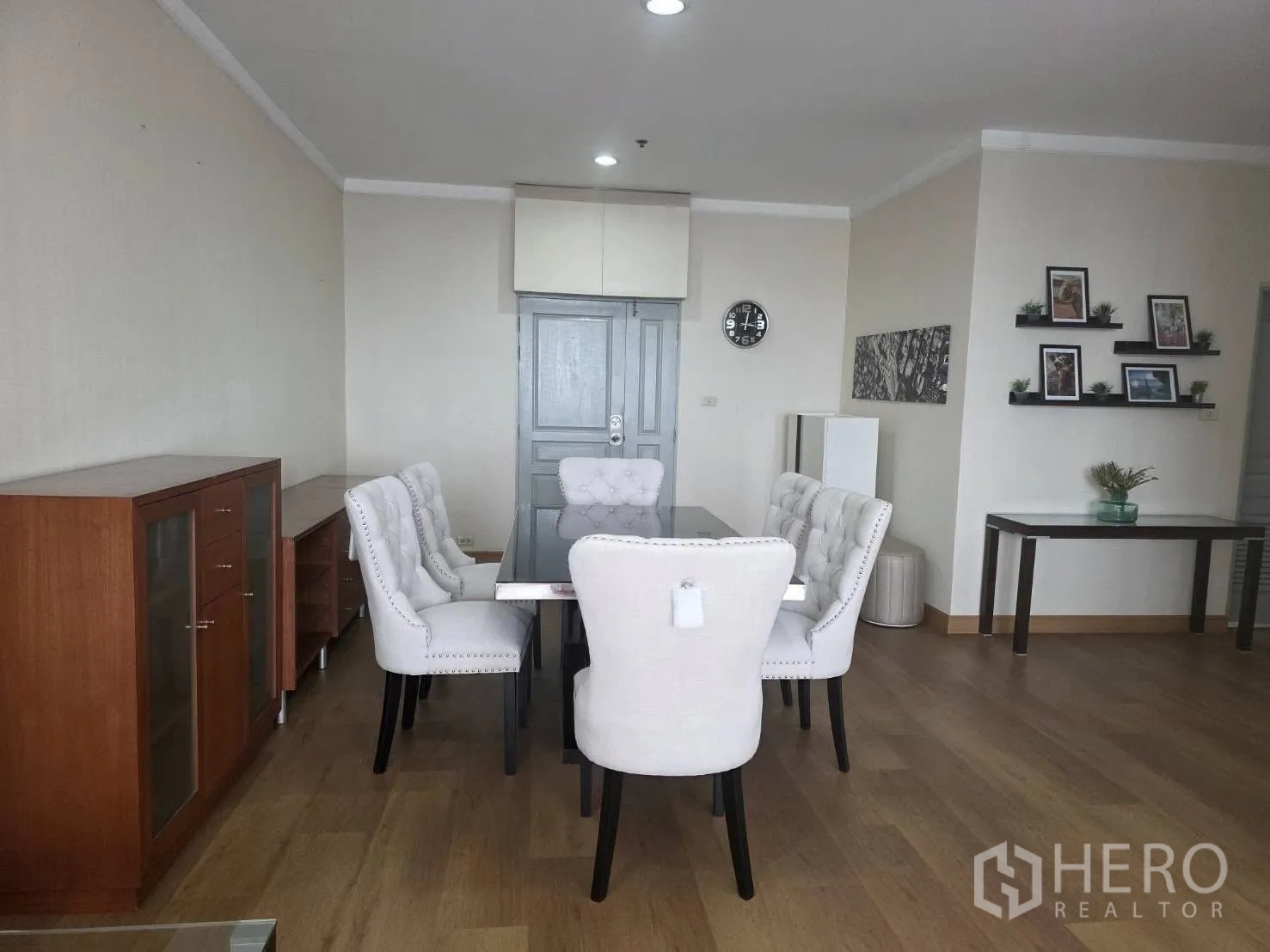 Condominium for rent in Khlong Toei, Bangkok - Formal dining area with six tufted chairs, wood flooring and wall shelves.