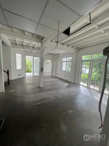独立式住宅 出租或出售在Sathon, Bangkok - 一层大开间，裸露梁架与水泥地面，落地玻璃门通往花园。