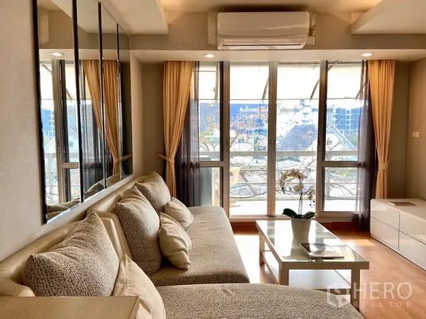 公寓 出售在Khlong Toei, Bangkok - 采光充足的客厅，落地窗通往阳台，转角沙发与茶几，位于BTS On Nut附近的Khlong Toei公寓。