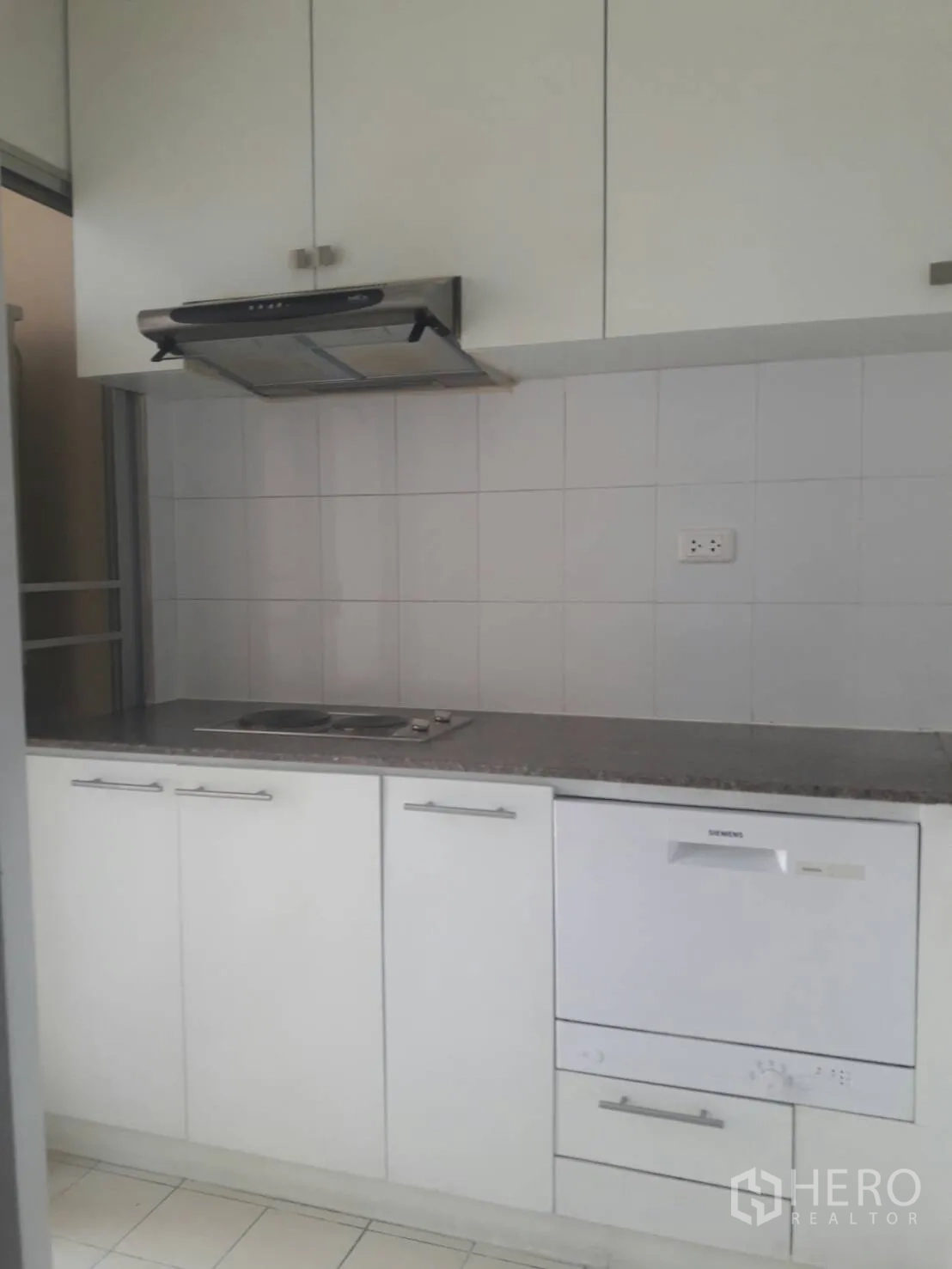 Condominium for rent in Khlong Toei, Bangkok - Separate galley kitchen with white cabinetry, cooktop, range hood, tiled splashback and a built-in dishwasher.
