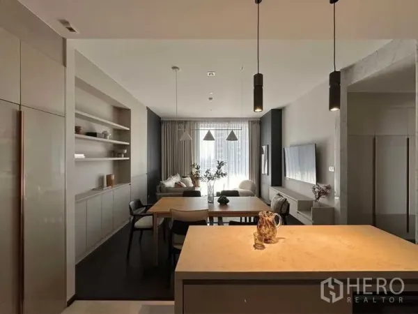 公寓 出租或出售在Watthana, Bangkok - 从厨房岛台望向餐客厅的全景，吊灯与电视墙一体。