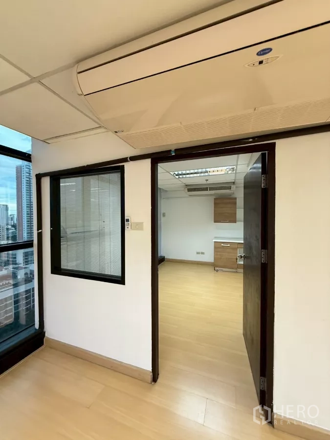 Office Space for rent in Watthana, Bangkok - Partitioned office room with split-type air conditioner over the doorway, light wood floors and a city-view window.
