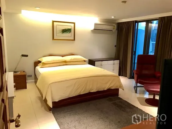 Condominium for rent in Bang Rak, Bangkok - Warm master bedroom with king bed, balcony access, red armchair and soft lighting.