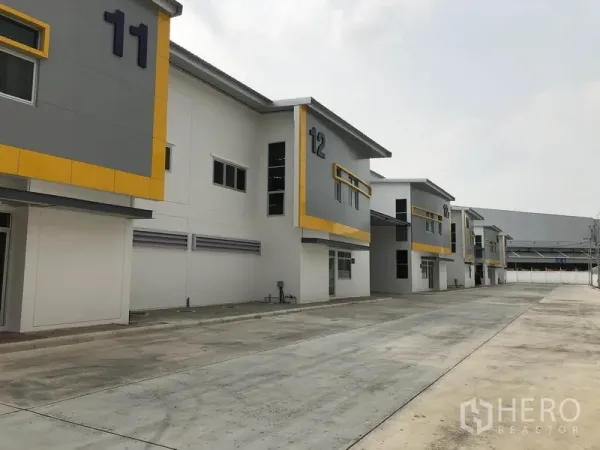Factory for rent in Phra Nakhon Si Ayutthaya - Row of modern factory units with numbers 11 and 12 and a wide truck‑friendly driveway.
