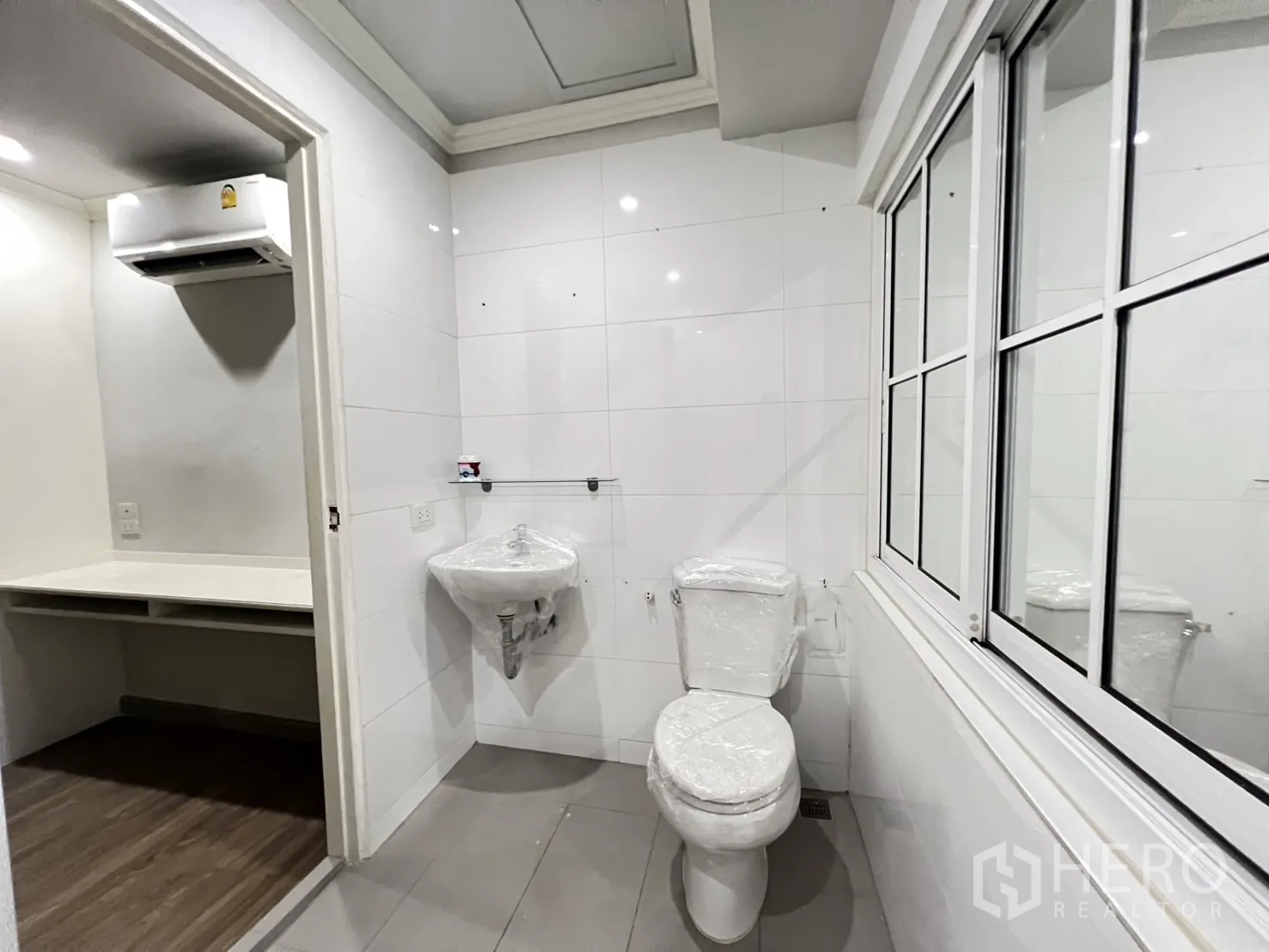 Shophouse for rent in Bang Rak, Bangkok - Small bathroom with toilet and basin beside a work nook with air conditioner.