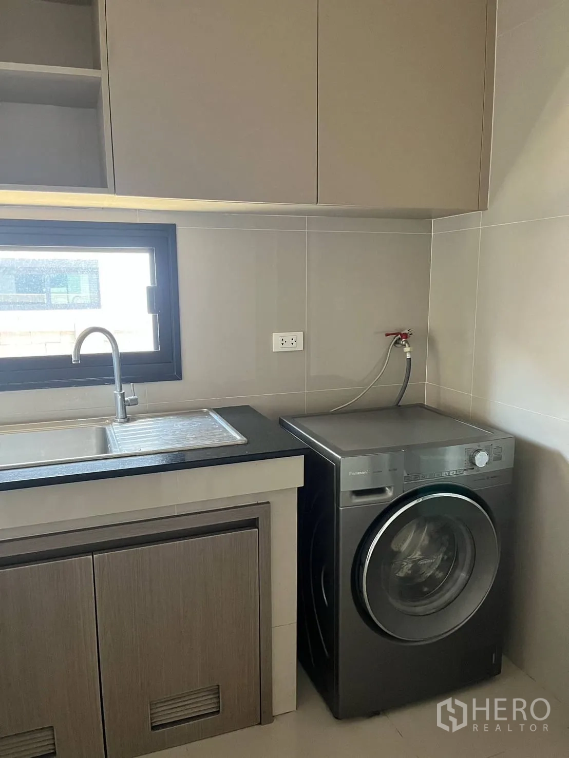Detached House for rent or sale in Lam Luk Ka, Pathum Thani - Laundry corner with front‑load washing machine beside sink and cabinets.
