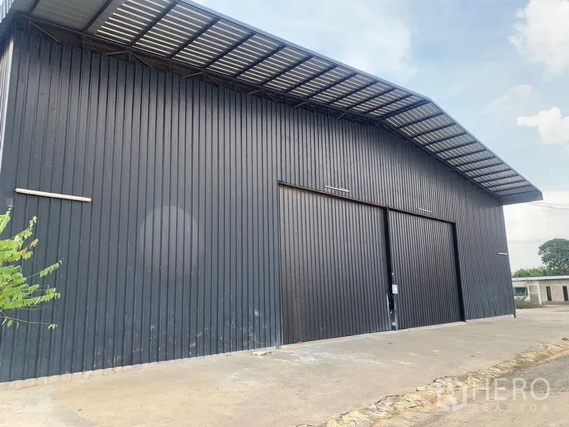 Warehouse for rent in Khan Na Yao, Bangkok - Modern black metal-clad warehouse exterior with wide sliding doors and a covered loading area.