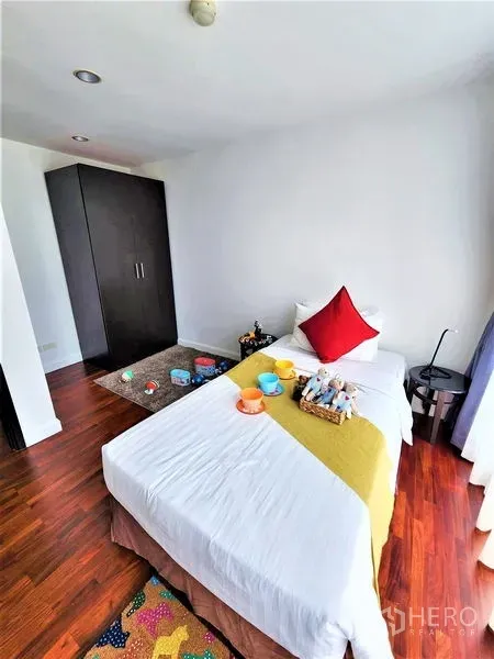 Condominium for rent in Bang Rak, Bangkok - Cozy bedroom with a single bed, dark wardrobe, and polished wooden floors.