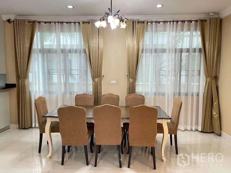 独立式住宅 出租在Mueang Nonthaburi, Nonthaburi - 餐厅设八人餐桌、枝形吊灯和大窗帘。