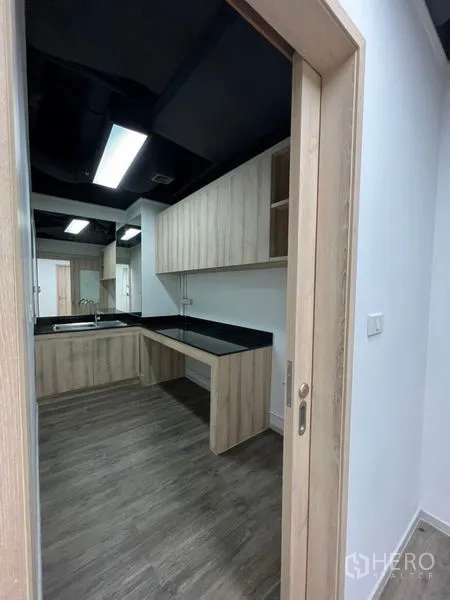 Office Space for rent in Khlong Toei, Bangkok - Pantry with L-shaped black countertop, sink and light wood cabinetry.