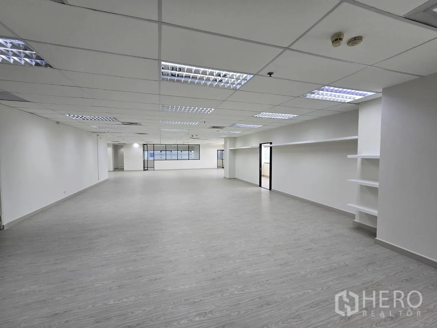 Office Space for rent in Khlong Toei, Bangkok - Spacious workspace with suspended ceiling lights, shelving, and multiple doorways.
