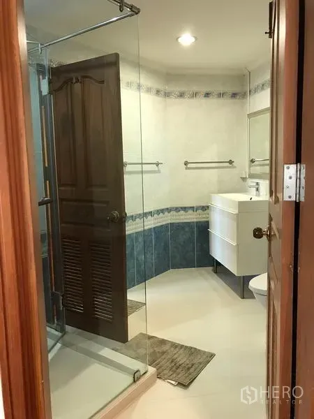 公寓 出租在Watthana, Bangkok - 浴室带玻璃淋浴间、白色洗手台与瓷砖墙面