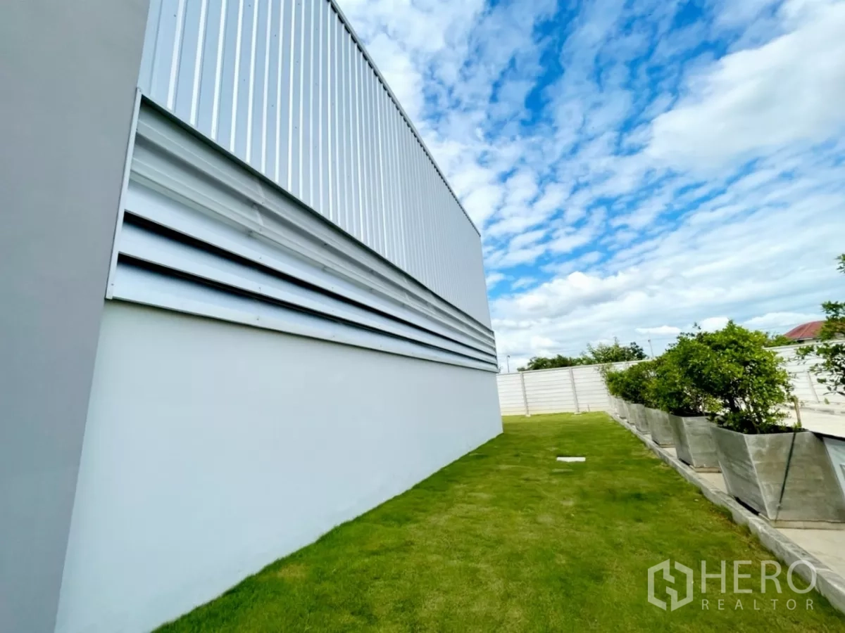 货栈 出售在Lam Luk Ka, Pathum Thani - 仓库外墙百叶与整洁草地、花盆的近景。