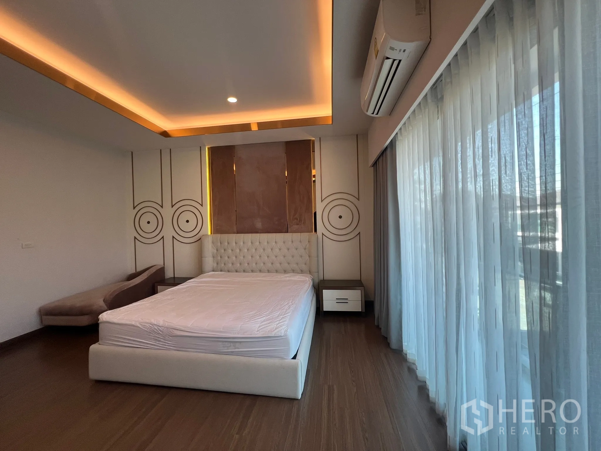 Detached House for rent or sale in Prawet, Bangkok - Master bedroom with tufted headboard, cove lighting and full-height windows.