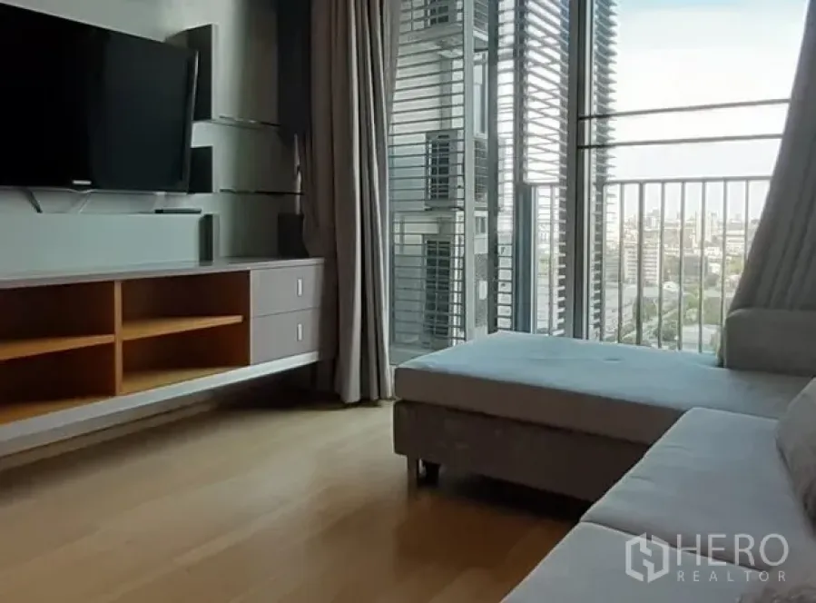 Condominium for rent in Khlong Toei, Bangkok - Bright living room with sofa, wall-mounted TV unit and balcony opening to a city view.