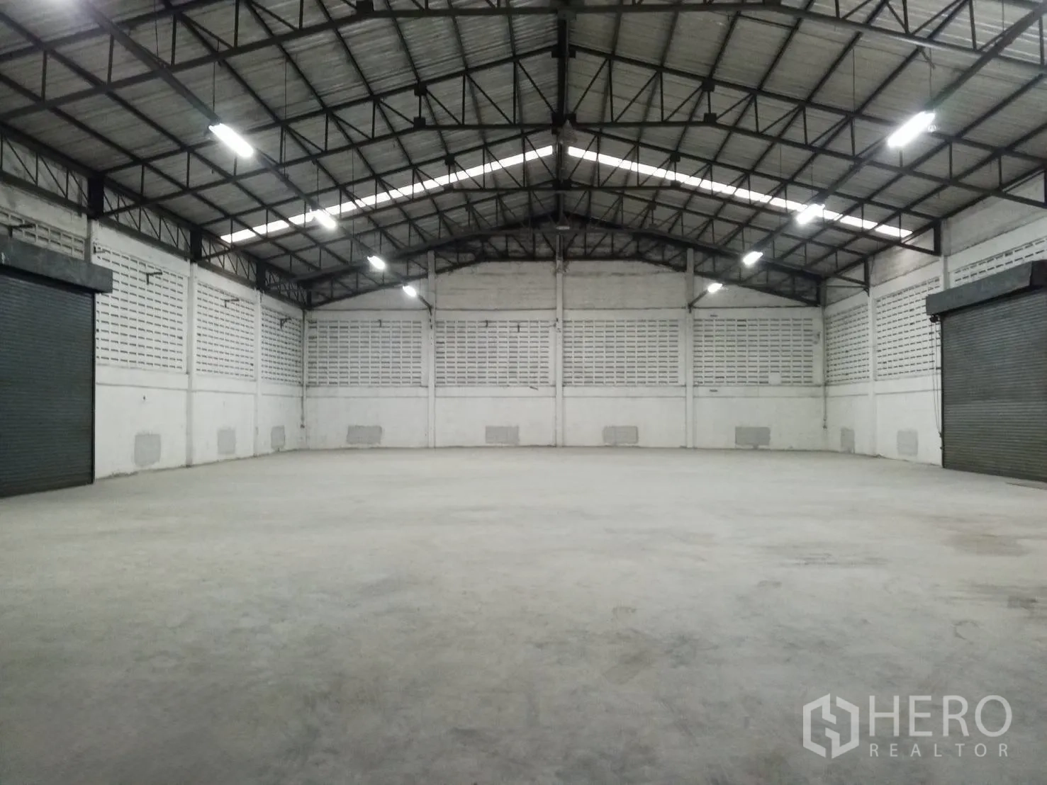 Warehouse for rent in Min Buri, Bangkok - Large open warehouse interior with high clearance, concrete slab and two roller shutter doors.