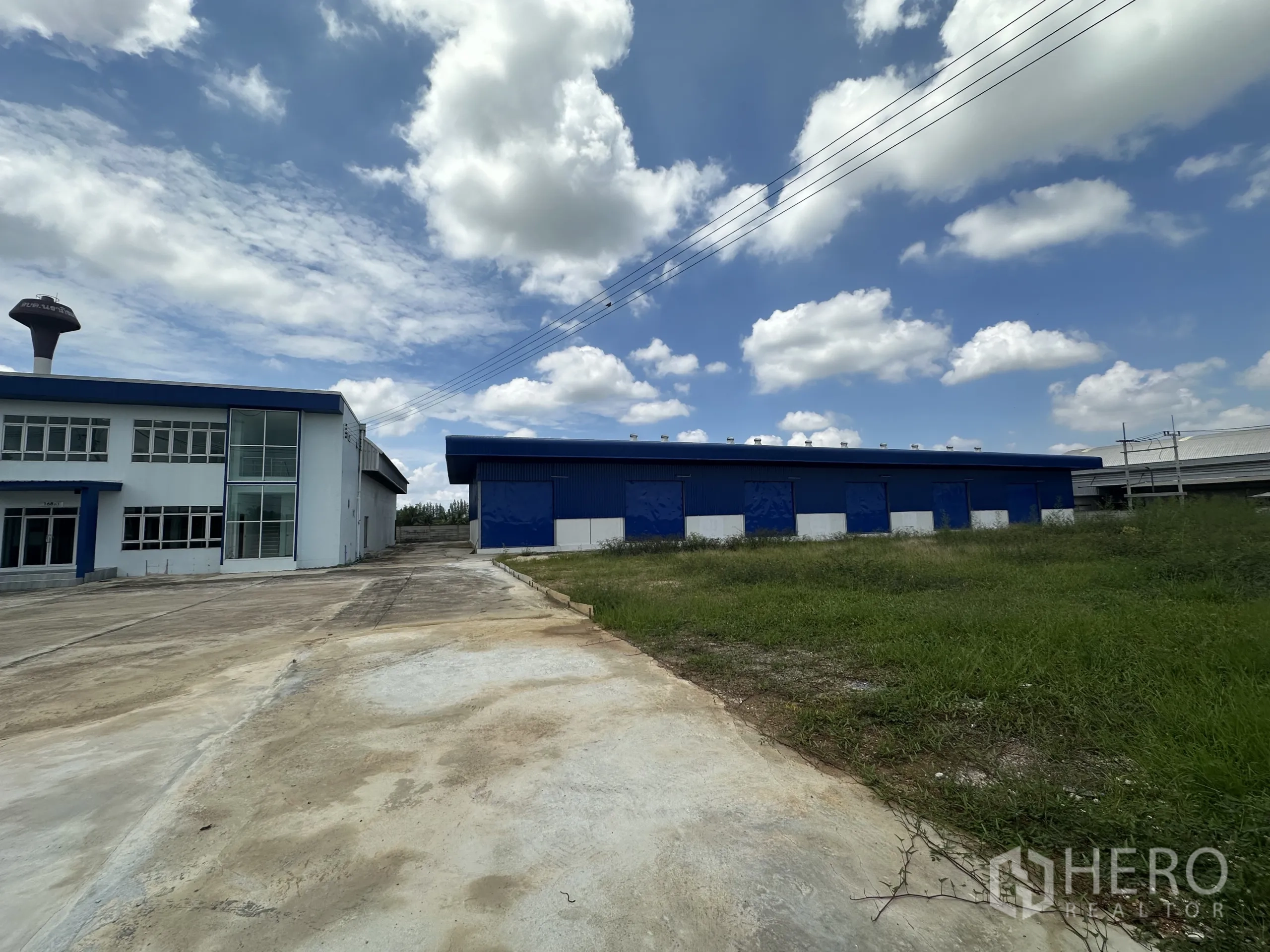 Warehouse for rent in Bang Len, Nakhon Pathom - Wide exterior view of office and warehouse with overhead power lines and open yard.