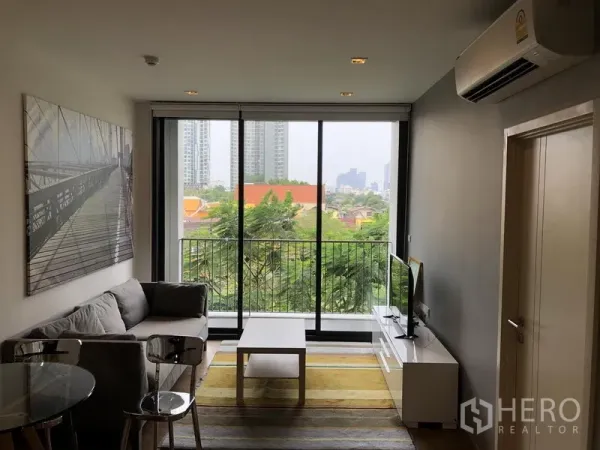 公寓 出租在Watthana, Bangkok - 采光充足的客厅，落地窗通往阳台，绿意城市景观。
