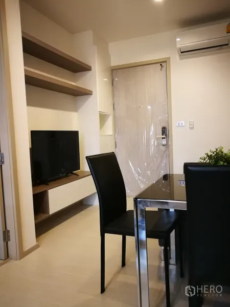 Condominium for rent in Khlong Toei, Bangkok - Compact living and dining area with wall-mounted shelves, TV console, and air conditioner.