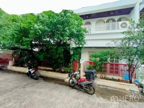 联排别墅 出租在Khlong Toei, Bangkok - 两层联排别墅外观，二层拱形窗、红色围栏与成树，街巷安静。