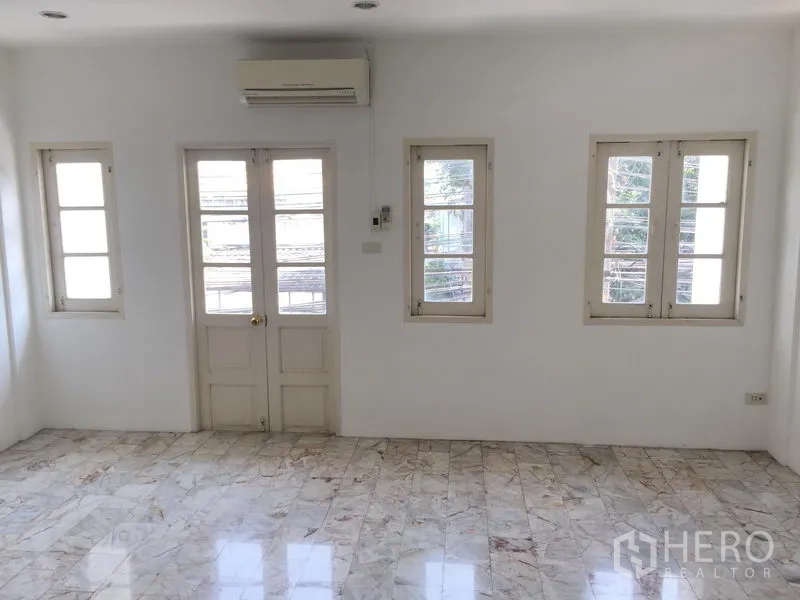 Townhouse for rent in Chatuchak, Bangkok - Sunlit bedroom with several windows, balcony doors and a wall-mounted air conditioner.